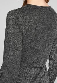 Svart klänning med ett strukturerat, glittrigt tyg. Har långa ärmar och en figursydd silhuett med en åtdragen midja och rundad halsringning.