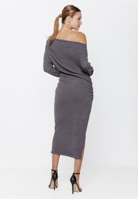 Szara, prążkowana sukienka midi na jedno ramię z marszczeniami i bocznymi rozcięciami, zestawiona z czarnymi szpilkami o gładkiej fakturze.