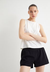 Top blanco sin mangas con una textura suave, combinado con pantalones cortos negros de cintura elástica, ambos con un ajuste relajado.