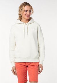 Crème-kleurige hoodie met een voorzak, een capuchon met trekkoord en geborduurde tekst "SPREAD LOVE AND BE HAPPY." Gepaard met koraalkleurige shorts.