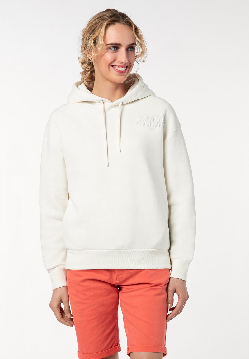 Crème-kleurige hoodie met een voorzak, een capuchon met trekkoord en geborduurde tekst "SPREAD LOVE AND BE HAPPY." Gepaard met koraalkleurige shorts.