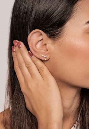 Silver stud earrings feature three small clear gemstones arranged in a delicate, clustered design. Smooth texture highlights the metallic shine.