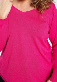 Kirkas vaaleanpunainen neulepaita, jossa on V-pääntie. Pehmeä neulepinta, pitkät hihat ja rento malli. Varustettu ribbatulla hihansuilla ja helmalla.