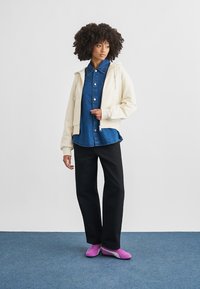 Κρεμ φούτερ με κουκούλα, πουκάμισο τζιν με κουμπιά, μαύρο παντελόνι και ροζ αθλητικά παπούτσια. Το ντύσιμο χαρακτηρίζεται από χαλαρή στρώση ρούχων και απαλές υφές υφάσματος.