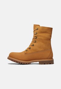 Bottes chelsea en suede marron avec un bout arrondi, six œillets en métal et une semelle en caoutchouc robuste avec des détails texturés sur les côtés.