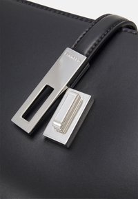 Sort læderhåndtaske med en sølv rektangulær lås og en mindre sølv hardware accent, samt synlige syninger på remmen.