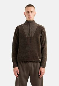 Maglione in maglia marrone con colletto alto, chiusura a mezza zip e motivo a costine verticali sulle spalle. Presenta un logo ricamato sull'orlo inferiore.