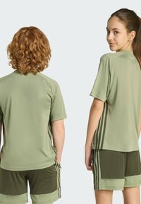 Zelené sportovní tričko s krátkými rukávy, bočními pruhy, ve spojení se zelenými šortkami se strukturovaným páskem a kapsami.