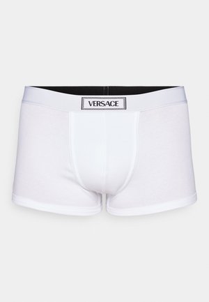 White cotton boxer briefs with a black elastic waistband, featuring a prominent Versace logo tag at the front center. Smooth texture.