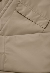 Bezs szövet sima felülettel; nagy zsebfedővel és átlós varrással díszítve. Külső ruházathoz alkalmas.