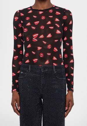 Zwart doorschijnend top met lange mouwen en een patroon van rode lippen, gecombineerd met zwarte, hooggetailleerde broek versierd met kleine zwarte kralen.
