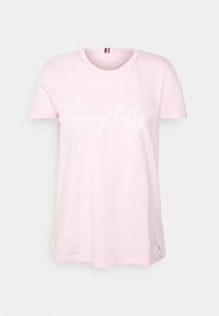 T-shirt in cotone rosa con collo rotondo, presenta un logo "Tommy Hilfiger" in bianco corsivo sul davanti. Maniche corte con una vestibilità rilassata.
