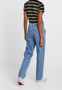 Jasnoniebieskie jeansy o wysokim stanie z luźnym krojem, wyposażone w dwie tylne kieszenie i minimalne przeszycia. W połączeniu z bluzką w czarno-żółte paski.