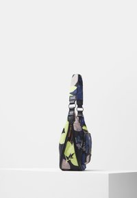 Kolorowa torebka na ramię w kwiatowy wzór z regulowanym paskiem i przednią kieszenią na zamek, prezentowana na białym postumencie.