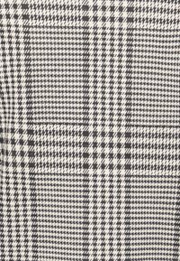 Černobílá tkanina s houndstooth vzorem se střídajícími se typy čtverců a čar, s texturovaným tkaným vzhledem.