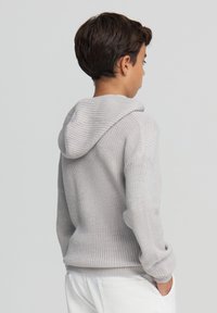 Jasnoszara dziana hoodie o teksturowanym wykończeniu, z długimi rękawami i dużą kieszenią z przodu. Miękki materiał i luźny krój.