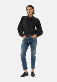 Chemise à manches longues noire à boutons avec un col ajusté et des manches bouffantes, associée à un jean en denim bleu et des mocassins noirs.