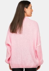 Overmaat roze gebreide trui met een losse, gestructureerde weving, brede mouwen en een ribbelzoom, die een relaxed fit en casual stijl laat zien.