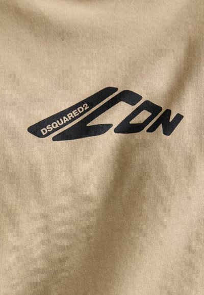 Beige stof med et fremtrædende sort "DSQUARED2" logo og stiliserede detaljer, der viser en glat tekstur og minimalistisk design.