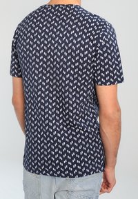 Camiseta de manga corta azul marino con un patrón blanco repetido de líneas verticales. Material de algodón, corte relajado, escote redondo.