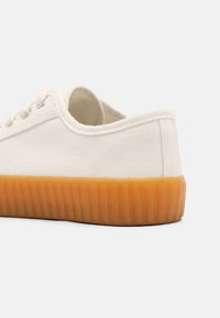 Canvas sneakers with a cream upper, featuring a textured rubber sole in amber, round laces, and minimalist design.