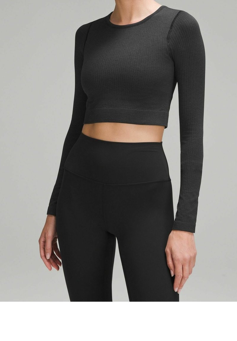 Schwarzes, geripptes Crop-Top mit langen Ärmeln, runder Ausschnitt und figurbetonte Silhouette, kombiniert mit hochtaillierten schwarzen Leggings.