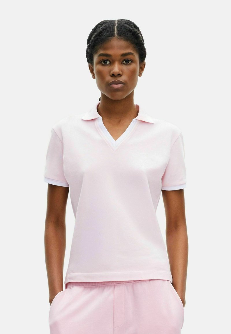 Lichtroze polo met een V-hals en korte mouwen. Beschikt over een geprofileerde stof en contrasterende witte kraag en manchetten.