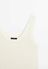 Débardeur en maille écru, avec un motif en diamant, des bretelles larges et un col côtelé. Étiquette affichée au centre.