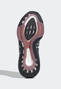 Suola di scarpa atletica nera e rosa con gomma testurizzata, fori circolari e ovali, e una intersuola bianca ammortizzata per un supporto aggiuntivo.