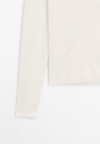 Maglione beige chiaro con una texture liscia, maniche lunghe, polsini a coste e orlo dritto. Design semplice e pulito senza motivi.