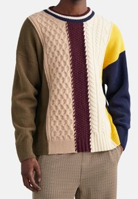 Maglione lavorato a maglia con un design in patchwork e motivi a trecce testurizzati in beige, borgogna, blu navy e giallo. Collo a girocollo e polsini a coste.