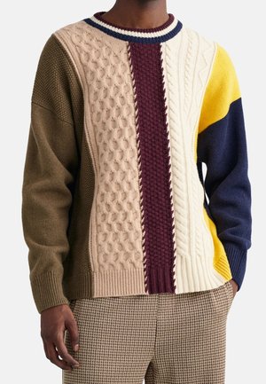 Suéter de punto con un diseño de patchwork y patrones de cable texturizados en beige, burdeos, azul marino y amarillo. Cuello redondo y puños acanalados.