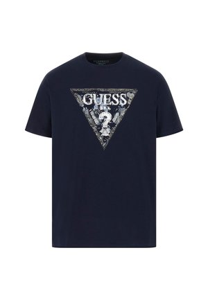 Marineblå bomulds t-shirt med en triangulær grafik, der har "GUESS" logo, spørgsmålstegn og blomsterdetaljer i hvid og sølv. Korte ærmer.