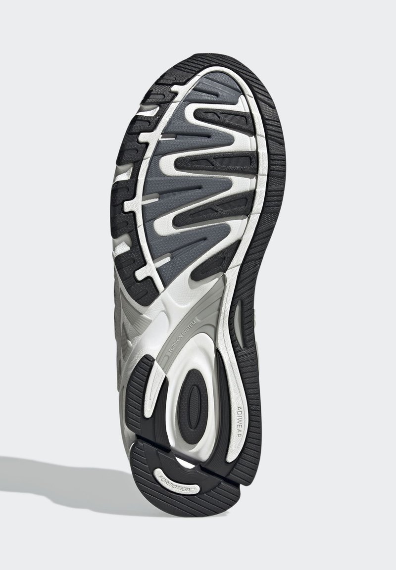 Suela de zapatilla deportiva en negro y gris con goma texturizada, ranuras para tracción y una forma amplia y redondeada que presenta un sistema de amortiguación visible.