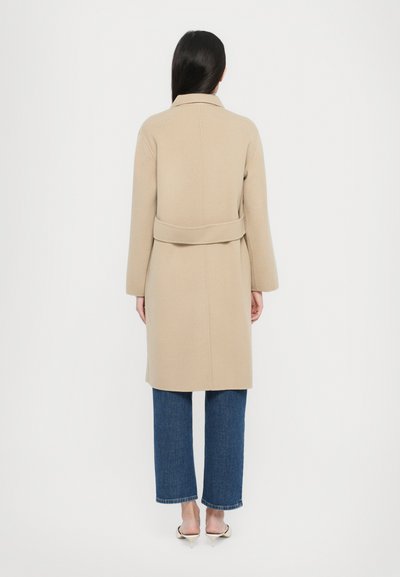 Beige wool coat with a belt, long sleeves, and a notched collar. Paired with blue wide-leg jeans and light-colored shoes.