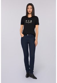 Černé tričko s krátkým rukávem a bílým logem "Trussardi", doplněné tmavě modrými úzkými džíny a černými kotníkovými botami.