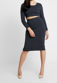 Pruhovaný dvoudílný outfit v tmavě modré a olivově zelené, sestávající z crop topu s dlouhými rukávy a přiléhavé midi sukně. Hladký, pružný materiál.