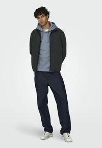 Dark jacket over a light blue hoodie, paired with dark denim jeans and white sneakers. Casual style with varied textures and colors.