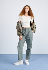Gray oversized pants with pleats, paired with a white crop top and a light green bomber jacket. White sneakers complete the outfit.