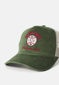 Gorra de pana verde con parte trasera de malla, con texto bordado en rojo "NUEVA YORK", gráfico de béisbol y detalle "Establecido en 1920".