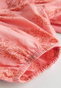 Rosa tyg med ett orange blommönster, samlad elastisk nederkant, mjuk textur och en slät yta. Lämplig för lätta kläder.
