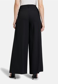 Zwarte wijde broek van vloeiende stof, met een hoge taille en een strak, tailormade ontwerp. De achterkant toont een gladde silhouet.