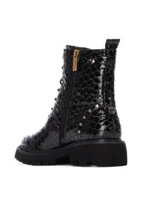 Botas negras hasta el tobillo con acabado de charol, textura de reptil, acentos de hardware dorado, cierre de cremallera y suela gruesa negra.