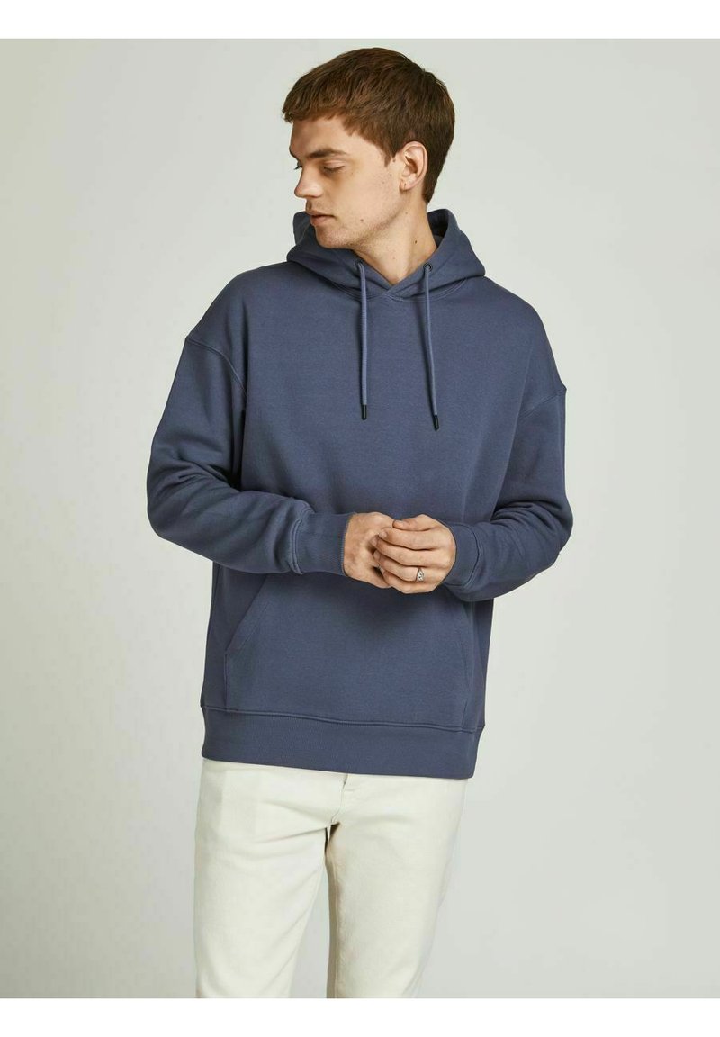 Dark blue hoodie made of soft fabric, featuring a front pocket, adjustable drawstring hood, and ribbed cuffs. Worn with light-colored pants.