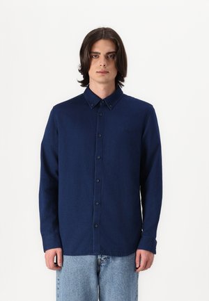 Camicia button-up blu scuro in un tessuto morbido, con colletto classico, maniche lunghe e un sottile dettaglio del logo sul petto.