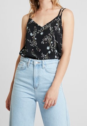 Woman wearing light blue high-waist jeans and a black floral sleeveless top with thin straps and a V-neckline.