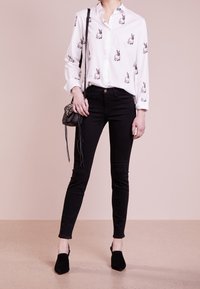 Camisa blanca con estampado de conejo negro, combinada con jeans negros ajustados y tacones de ante negros. Bolso cruzado negro con detalle de flecos.