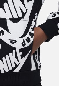 Mustahdud ja musta särgiga, millel on julged Nike logod ja tekstimustrid, koos eesoleva kukekotiga ja soonikkätistega, mis tagab mugava ja istuva välimuse.