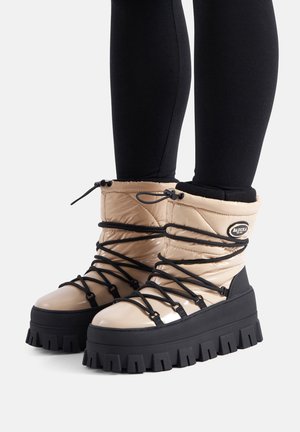 Beżowe, puchate botki do kostki z grubą, czarną podeszwą. Posiadają czarne sznurówki i akcenty, błyszczące wykończenie oraz zaokrąglony kształt noska.