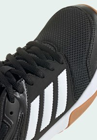 Sneaker nero con superficie testurizzata, caratterizzata da una punta liscia nera, marchio a tre strisce bianco e suola in gomma color caucciù.